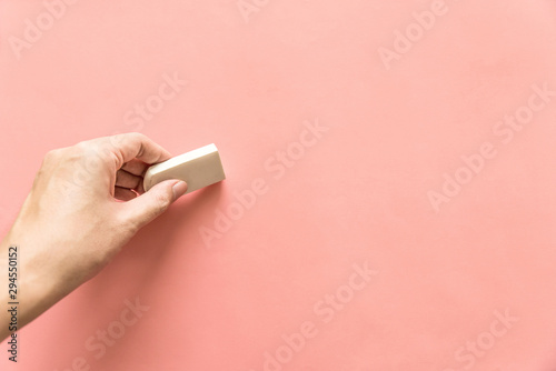 Hand holding white rubber for erasing something on empty pink background. Abstract background with copy space. photo