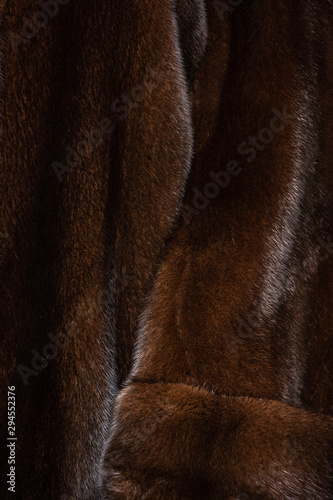 Natural dark brown shiny fur texture with beautiful pleats in the form of waves and part of the sleeve