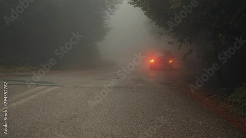 Approaching stranded car in foggy forest road.A stopped car in the middle of the foggy forest road.Someone is approaching.Crime,emergency,or halloween concept.
