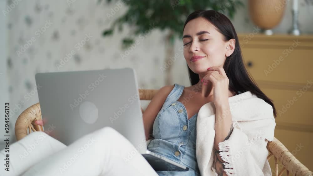 Beautiful young woman sits in armchair and works on laptop, freelance