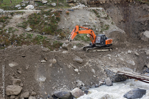 Orange excavator in gray mountains near river. Construction concept
