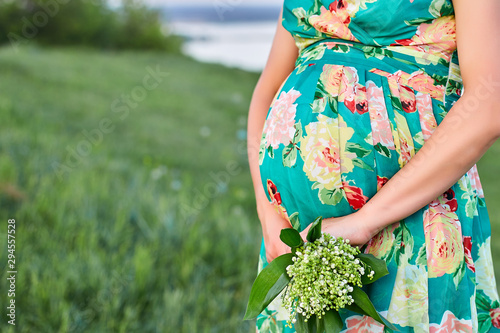 Pregnant woman holding her belly and flower, outdoor. Pregnancy, motherhood and happy future mother concept.