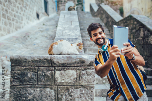 Young handsome tourist men using digital tablet in a city, make selfie with cat, having fun.