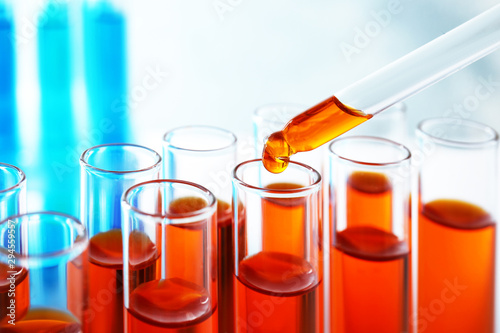 Dropping sample into test tube with orange liquid, closeup