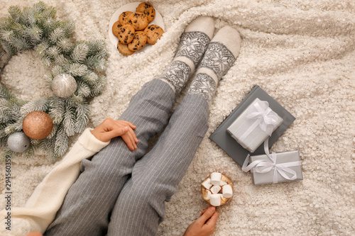 Young woman with cocoa and cookies sitting on light blanket, top view. Christmas holiday