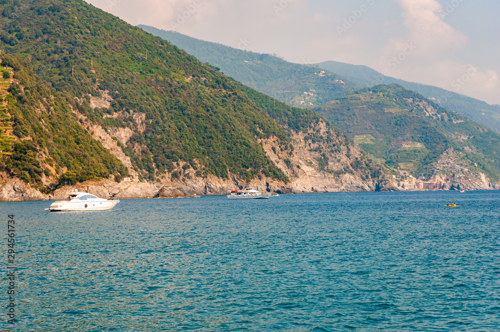 Sea yachts and boats traveling near the rocky coastline with green mountains on the background in Monterosso Al Mare, Cinque Terre