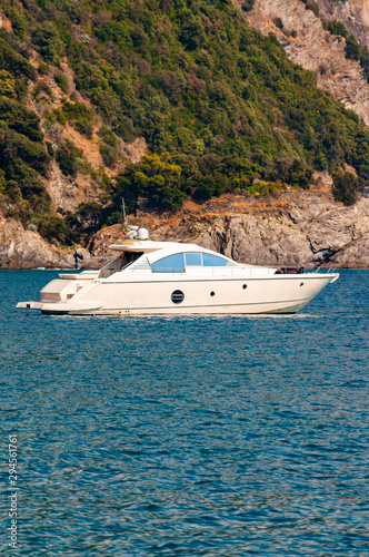 White luxury sea boat floating near the rocky coastline with green mountains on the background in Monterosso Al Mare, Cinque Terre