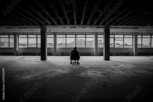 Man sitting in front of a large window in an empty hall of an abandoned building - black and white