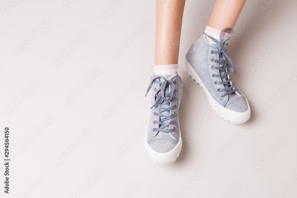 Pastel blue sneakers on legs. Casual footwear on grey. Pastel blue sneakers on legs. Casual footwear on grey.