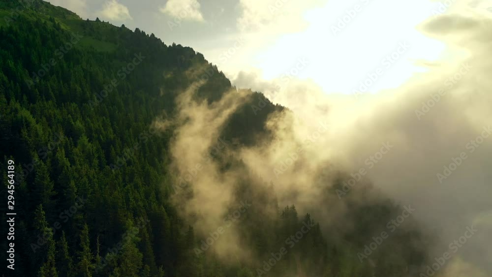 Aerial, reverse, drone shot, over a split view, over forest and through fog clouds, at sunrise, on a sunny and foggy, summer morning, in the Swiss alps of Valais, Switzerland Aerial, reverse, drone shot, over a split view, over forest and through fog clouds, at sunrise, on a sunny and foggy, summer morning, in the Swiss alps of Valais, Switzerland