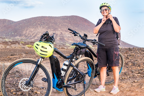 A pretty senior woman closes the yellow helmet before starting the off-track route. Go with electric bicycle with battery and motor can help you in the most difficult passages. A healthy lifestyle