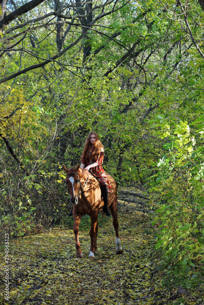 Red haired beautiful cowgirl bareback ride her horse in autumn country road at sunset Red haired beautiful cowgirl bareback ride her horse in autumn country road at sunset