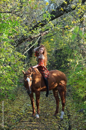 Red haired beautiful cowgirl bareback ride her horse in autumn country road at sunset