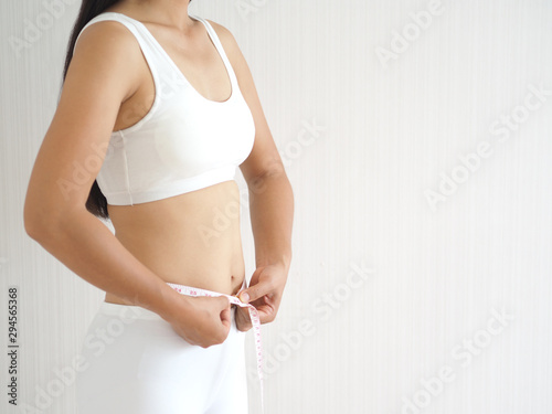 weight loss and slim body in asian woman with wrapped around her waistline by tape measure use for workout,fitness or diet and burn,block or detox and dietary supplement product on white background.