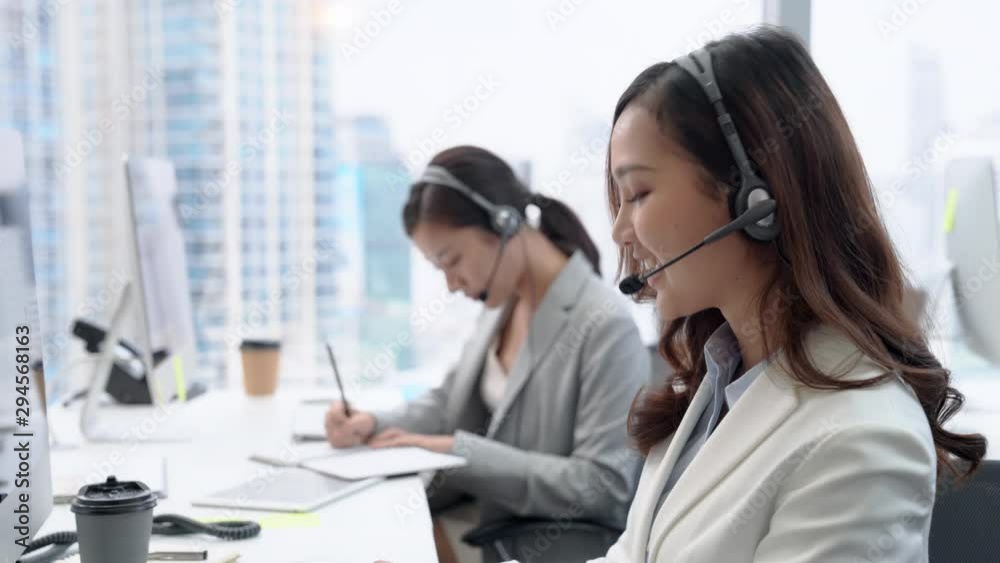 Smiling beautiful Asian woman working in call center office as a customer service operator with colleague