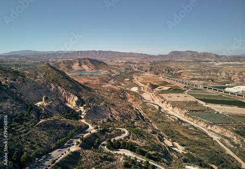 Aerial photography countryside with agricultural fields and meadows, artificial lake, waving roads and rocky mountains of Novelda, town located in province of Alicante, Spain