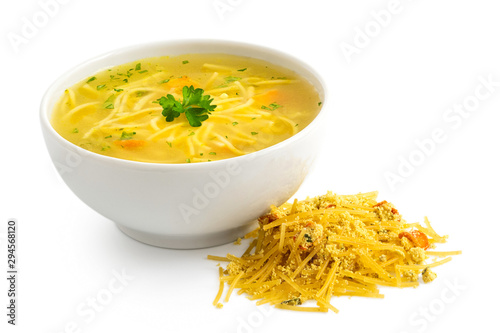 Instant chicken noodle soup in a white ceramic bowl next to a pile of dry instant soup isolated on white. Parsley garnish.