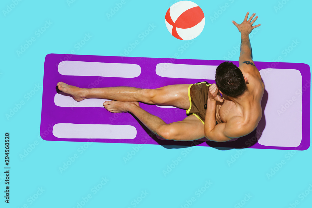 Top view of young caucasian male model's resting on beach resort on purple mat and blue background. Man's lying under sunlight and talking on phone. Concept of summertime, party, chill, vacation. Top view of young caucasian male model's resting on beach resort on purple mat and blue background. Man's lying under sunlight and talking on phone. Concept of summertime, party, chill, vacation.