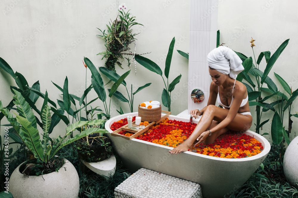 Woman relaxing in outdoor bath with flowers in Bali spa hotel. - obrazy, fototapety, plakaty 
