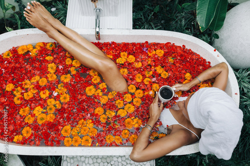 Fotografia Woman relaxing in outdoor bath with flowers in Bali spa hotel.