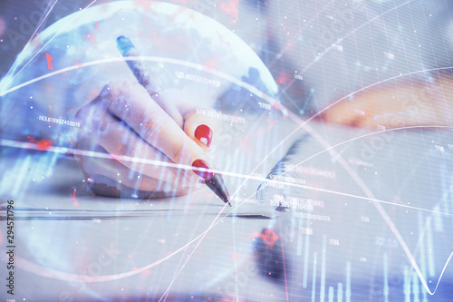 Double exposure of woman's hands making notes with forex graph hologram. Concept stock market analysis.