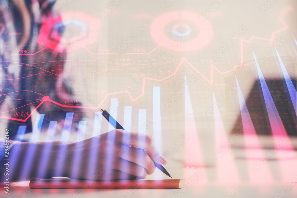 A woman hands writing information about stock market in notepad. Forex chart holograms in front. Concept of research. Double exposure