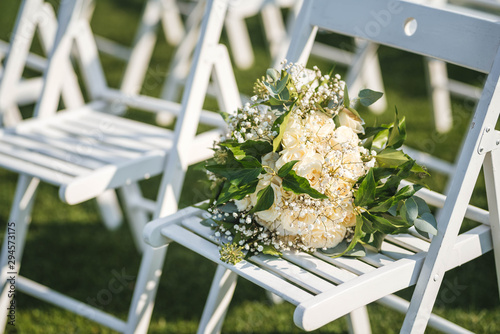 Wedding bouquet made of white roses and greenery on a chair. Outdoor weddng ceremony photo