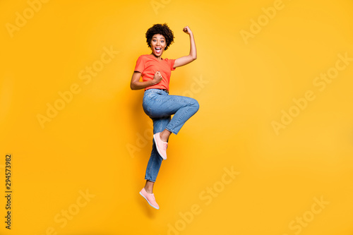 Fototapeta Naklejka Na Ścianę i Meble -  Full length body size photo of cheerful cute black girlfriend jumping up wearing jeans denim t-shirt footwear rejoicing isolated over yellow vivid color background