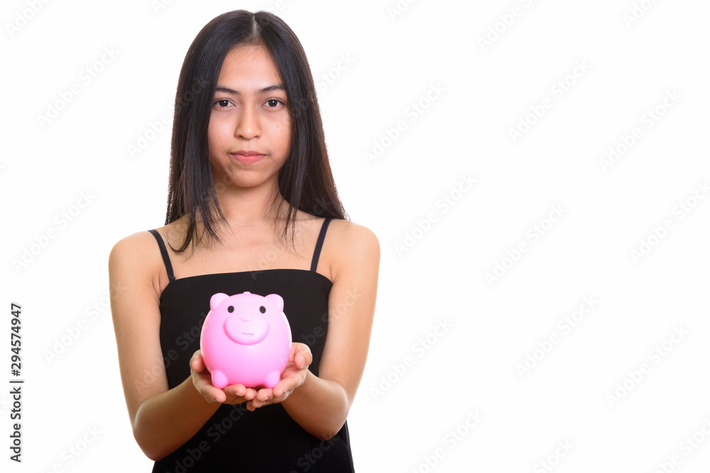 Studio shot of young Asian teenage girl holding piggy bank