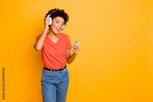 Copyspace photo of cheerful cute nice charming casual trendy attractive girlfriend black skinned wearing t-shirt jeans denim holding phone in her hand isolated over yellow bright color background