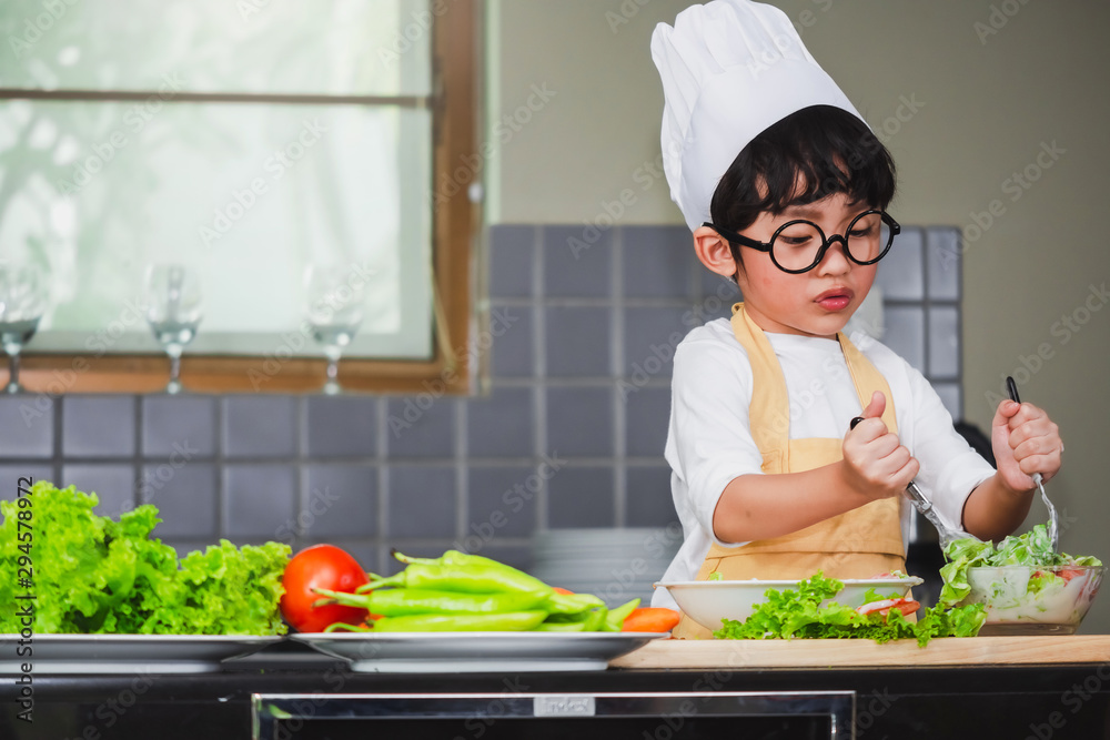 Asian Boy son cooking salad food holdind wooden spoon with vegetable holding tomatoes and carrots, bell peppers on plate for happy family cook food enjoyment lifestyle kitchen in home Asian Boy son cooking salad food holdind wooden spoon with vegetable holding tomatoes and carrots, bell peppers on plate for happy family cook food enjoyment lifestyle kitchen in home