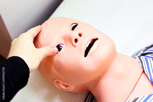 The head of a lying training dummy imitating a man with an open mouth and female hand opening its eye
