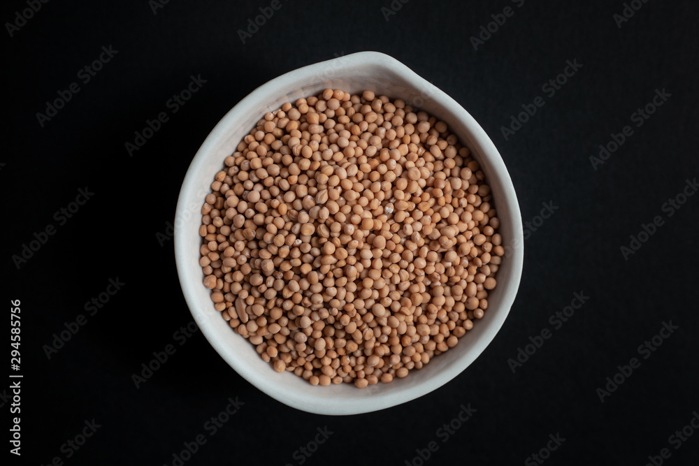 Mustard seeds spice in white ceramic bowl isolated on black background Mustard seeds spice in white ceramic bowl isolated on black background