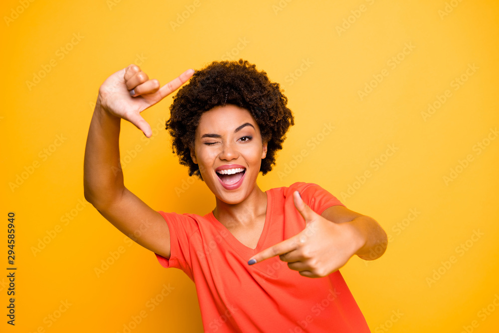 Photo of curly wavy cheerful charming lady wearing orange t-shirt pretending to take self photo shaping frame with her fingers isolated over yellow vivid color background Photo of curly wavy cheerful charming lady wearing orange t-shirt pretending to take self photo shaping frame with her fingers isolated over yellow vivid color background