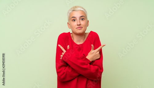 Teenager girl with white short hair over green wall pointing to the laterals having doubts