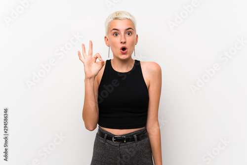 Teenager girl with short hair over white wall surprised and showing ok sign