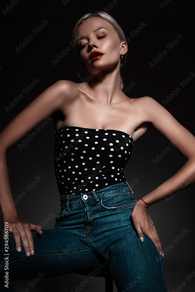 Portrait of hot sexy girl with beautiful blonde hair in underwear and jeans posing on chair in room on black background. Seductive fashion stylish woman model Portrait of hot sexy girl with beautiful blonde hair in underwear and jeans posing on chair in room on black background. Seductive fashion stylish woman model