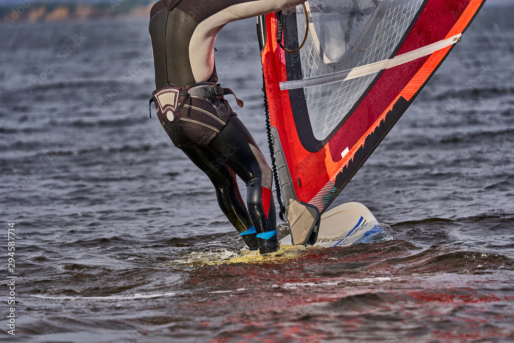 Naklejka premium A male athlete is interested in windsurfing. He moves on a Sailboard on a large lake on an autumn day.