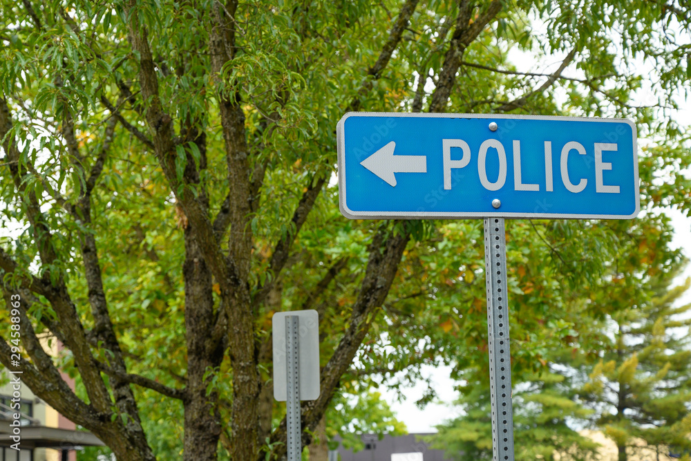 Police sign with arrow. On a green tree background.