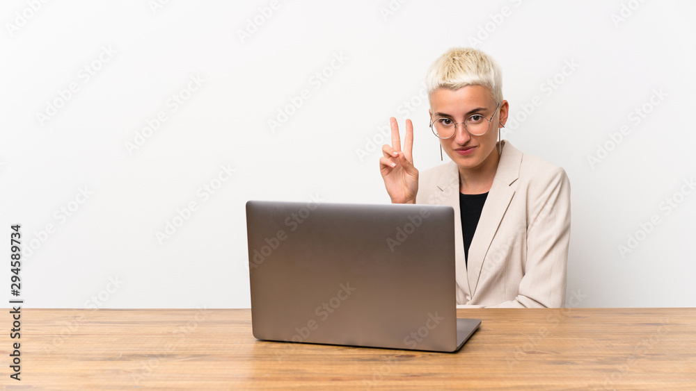 Teenager girl with short hair with a laptop smiling and showing victory sign