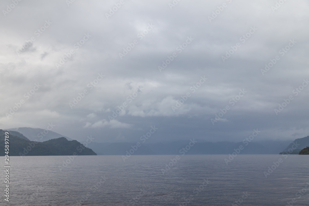 Cloudy gray landscape on a lake or sea in the Altai mountains during the rain in autumn or summer. Loneliness, nature, bad weather, water.