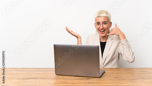 Teenager girl with short hair with a laptop making phone gesture and doubting