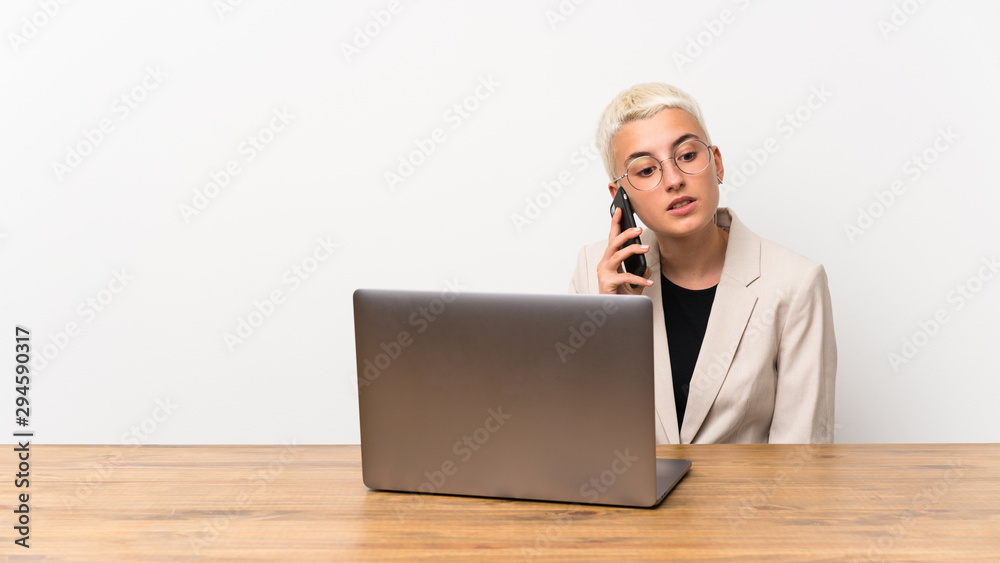 Teenager girl with short hair with a laptop keeping a conversation with the mobile phone Teenager girl with short hair with a laptop keeping a conversation with the mobile phone