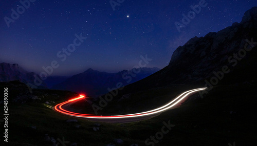 Fotografie TIMELAPSE: Car lights create a blurry trail leading through mountains at night