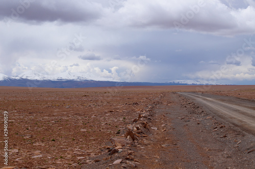 A road in the landscape of the Bolivian highlands. Desert landscape of the Andean plateau of Bolivia with the peaks of the snow-capped volcanoes of the Andes