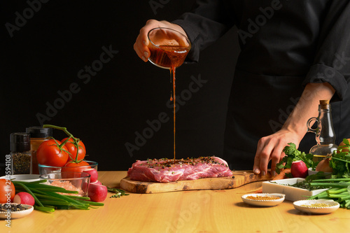 Chef cooks pork steak. pouring sauce, marinade on a background with vegetables. Recipe book, cooking, restaurant business