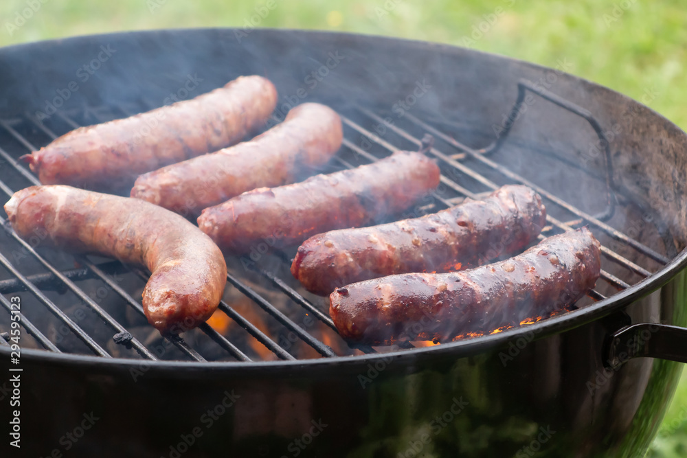 Cooking meat sausages on a round grill outdoors on a summer day