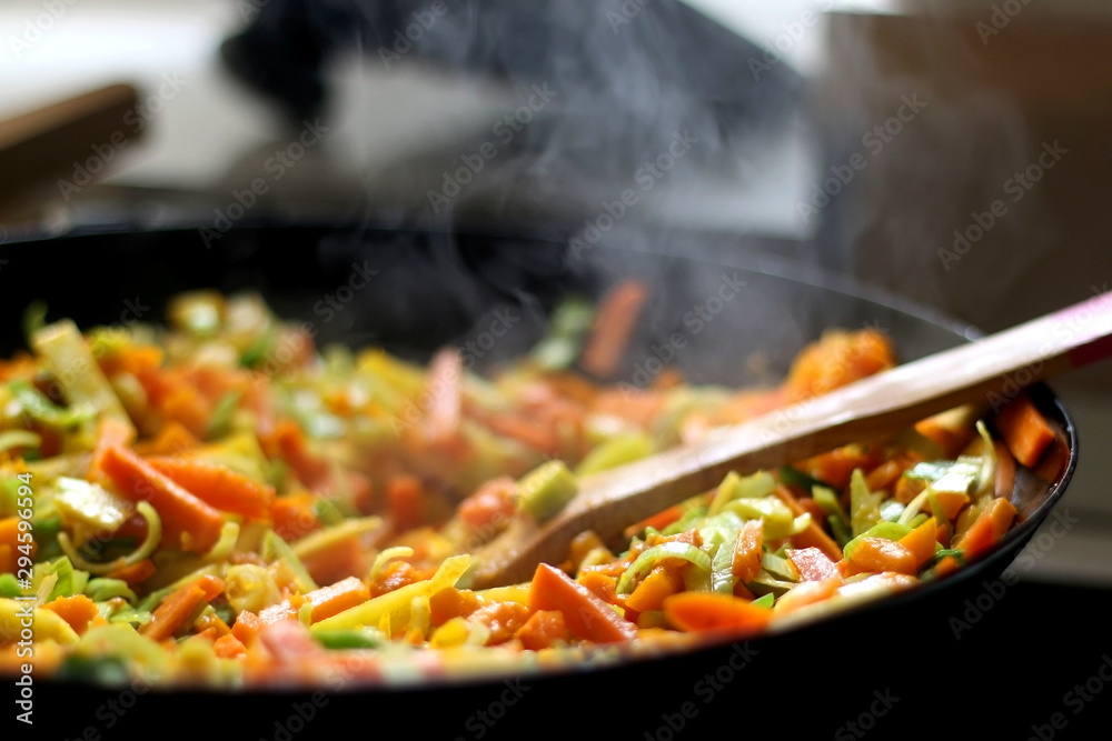 Cooking carrot, pumpkin, zucchini nad leek in wok. Selective focus, close-up.