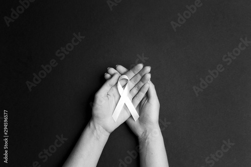 Female hands holding white ribbon on black background. November lung cancer awareness month.