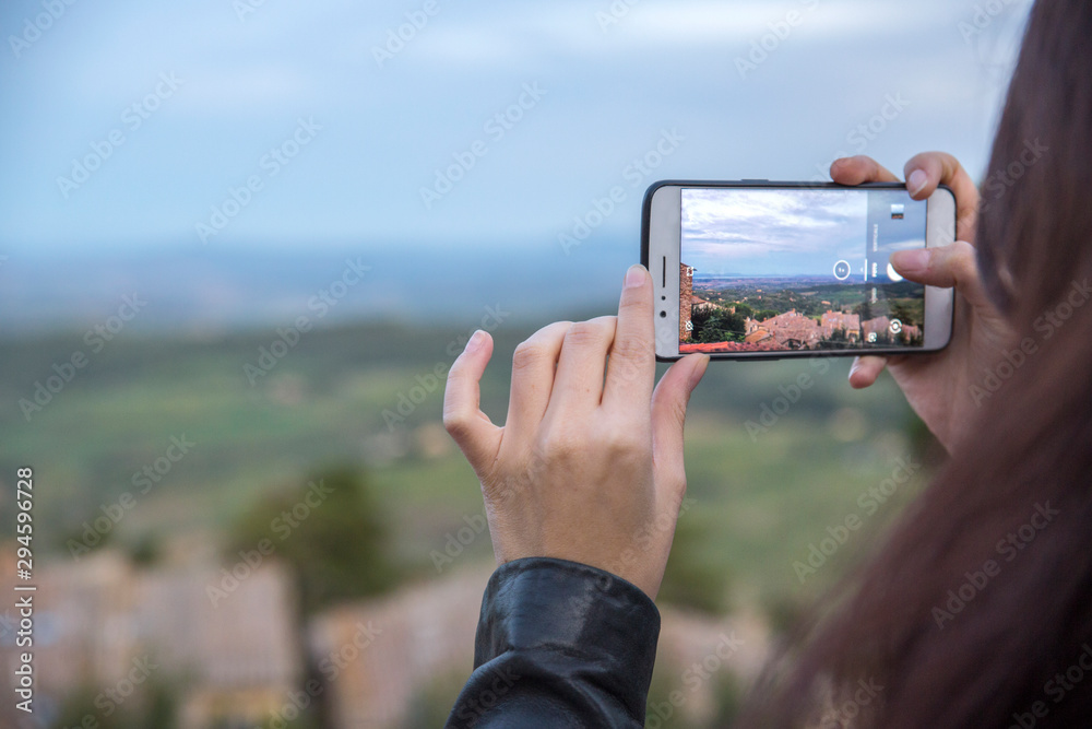Detail of the hands of a girl taking a picture from her smartphone. In the background a countryside panorama.